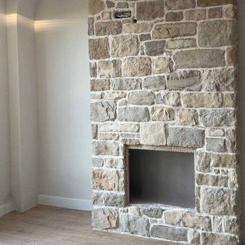 Stone fireplace with light-colored irregular stones and a rectangular firebox in a living room setting, wooden floor nearby