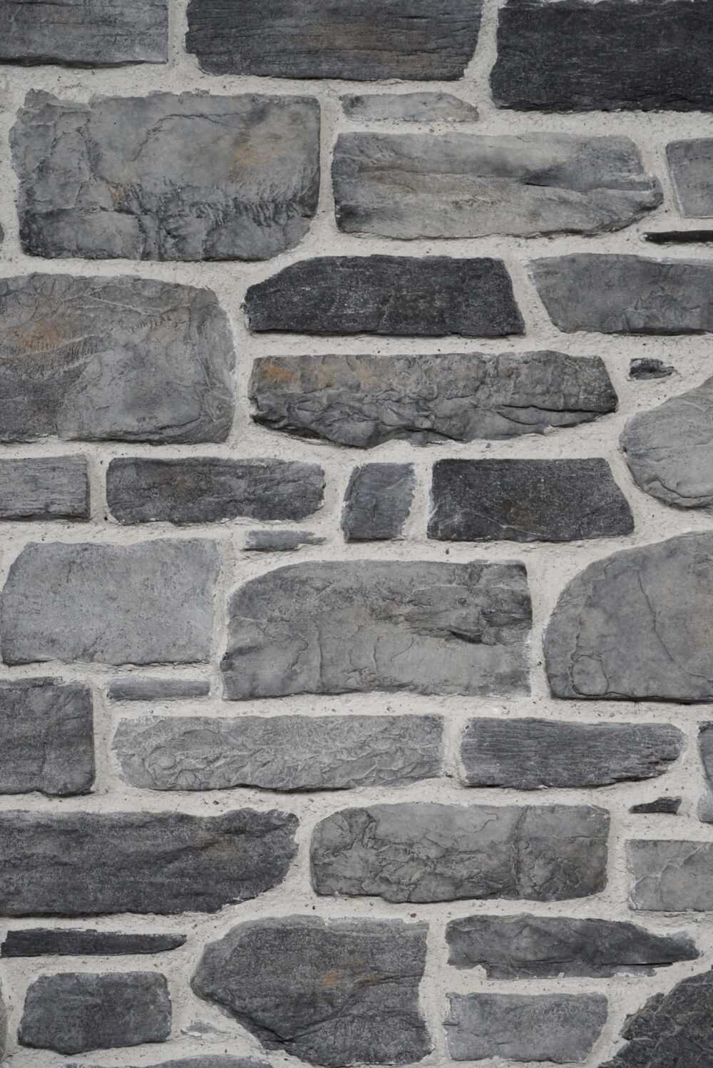 Gray stone wall with irregular rectangular bricks and light mortar between them.