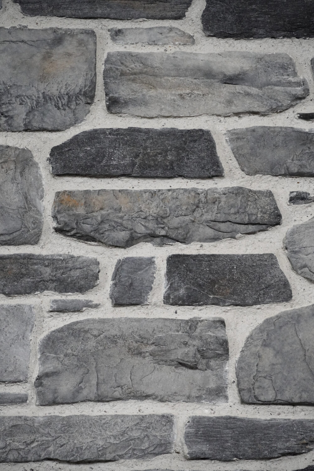 Close-up of a gray stone wall with irregular rectangular stones and light mortar across joints.