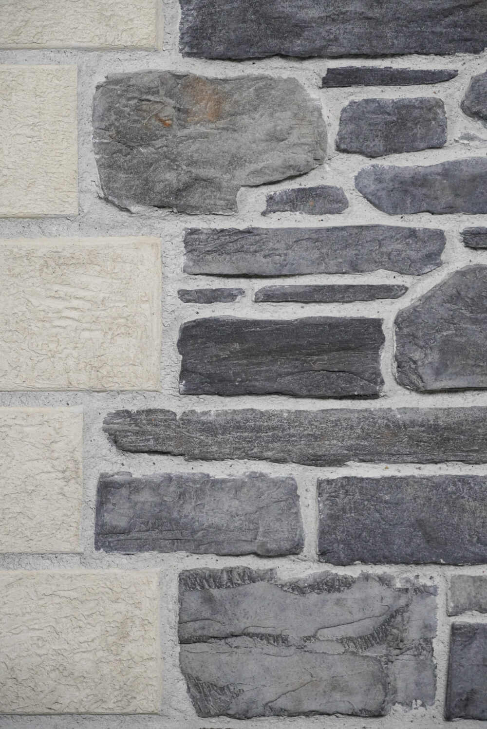 Exterior stone wall with beige rectangular blocks and dark gray stones set in light mortar.
