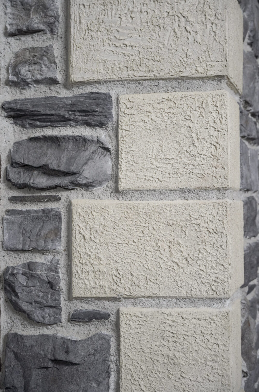 Stone wall with rectangular beige blocks and dark gray slate stones, textured masonry pattern.