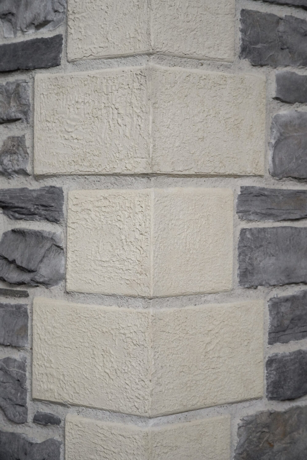 Close-up of a beige, rough-textured stone wall with darker gray stones on the sides.