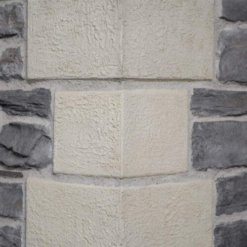 Close-up of a beige, rough-textured stone wall with darker gray stones on the sides.