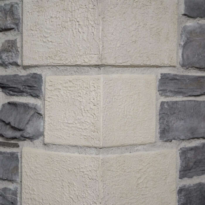Close-up of a beige, rough-textured stone wall with darker gray stones on the sides.