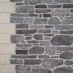 Stone wall made of irregular gray stones with a beige stone column along the left edge.