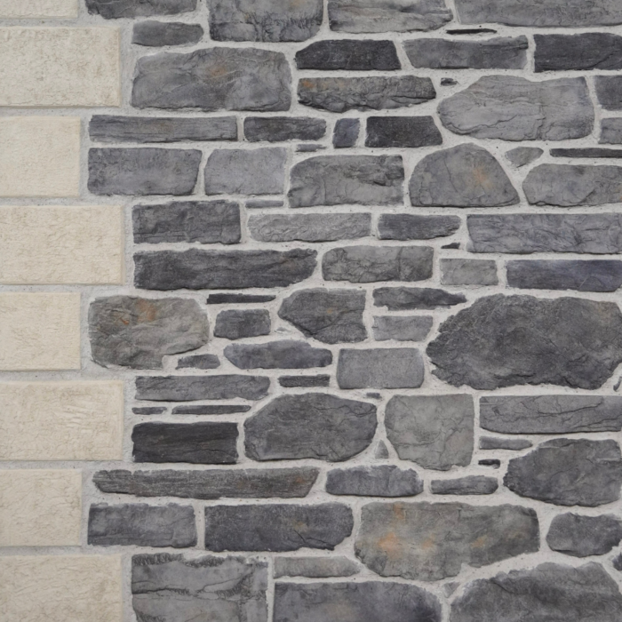 Stone wall made of irregular gray stones with a beige stone column along the left edge.